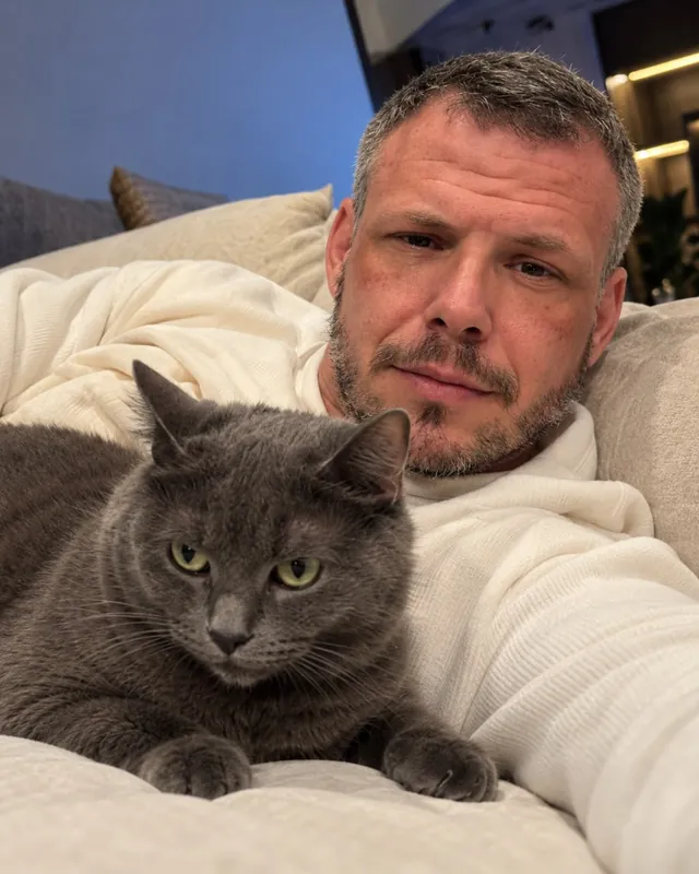Ben Parker at home on the sofa with his grey cat